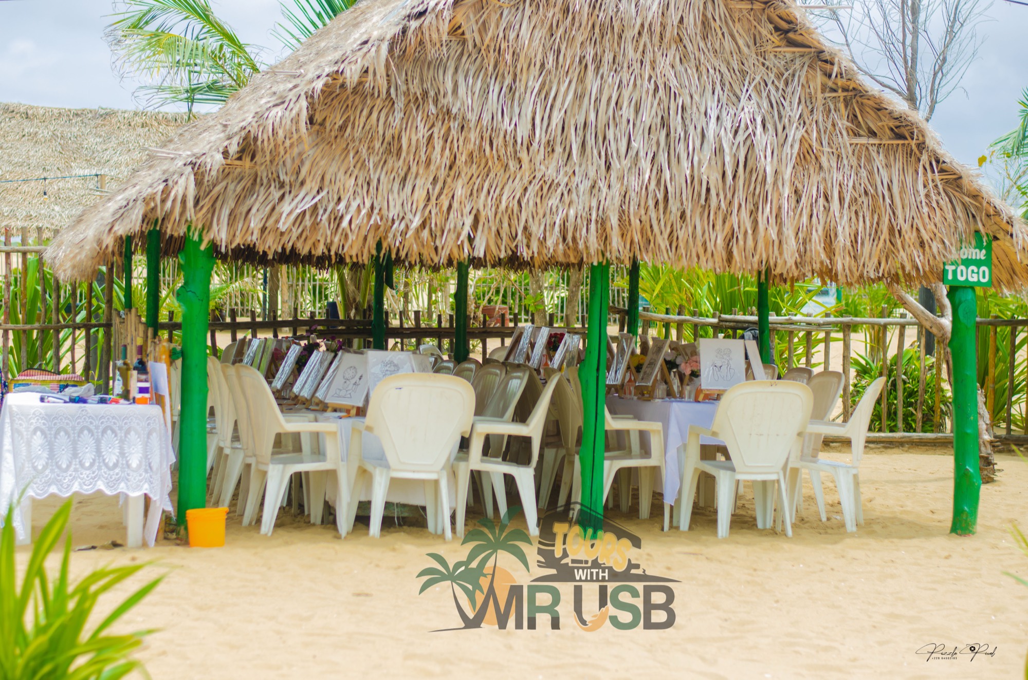 Easels and long tables set up under a thatched beach paillote before the Sip & Paint begins